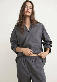 Pijama gris de tela suave, con una camisa de botones que incluye un bolsillo y pantalones con cintura elástica, en un corte relajado.
