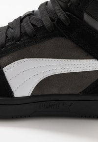 Svart mocka högsko som har ett framträdande vitt läderstreck, texturerade snören och en svart gummisula med logodetalj.