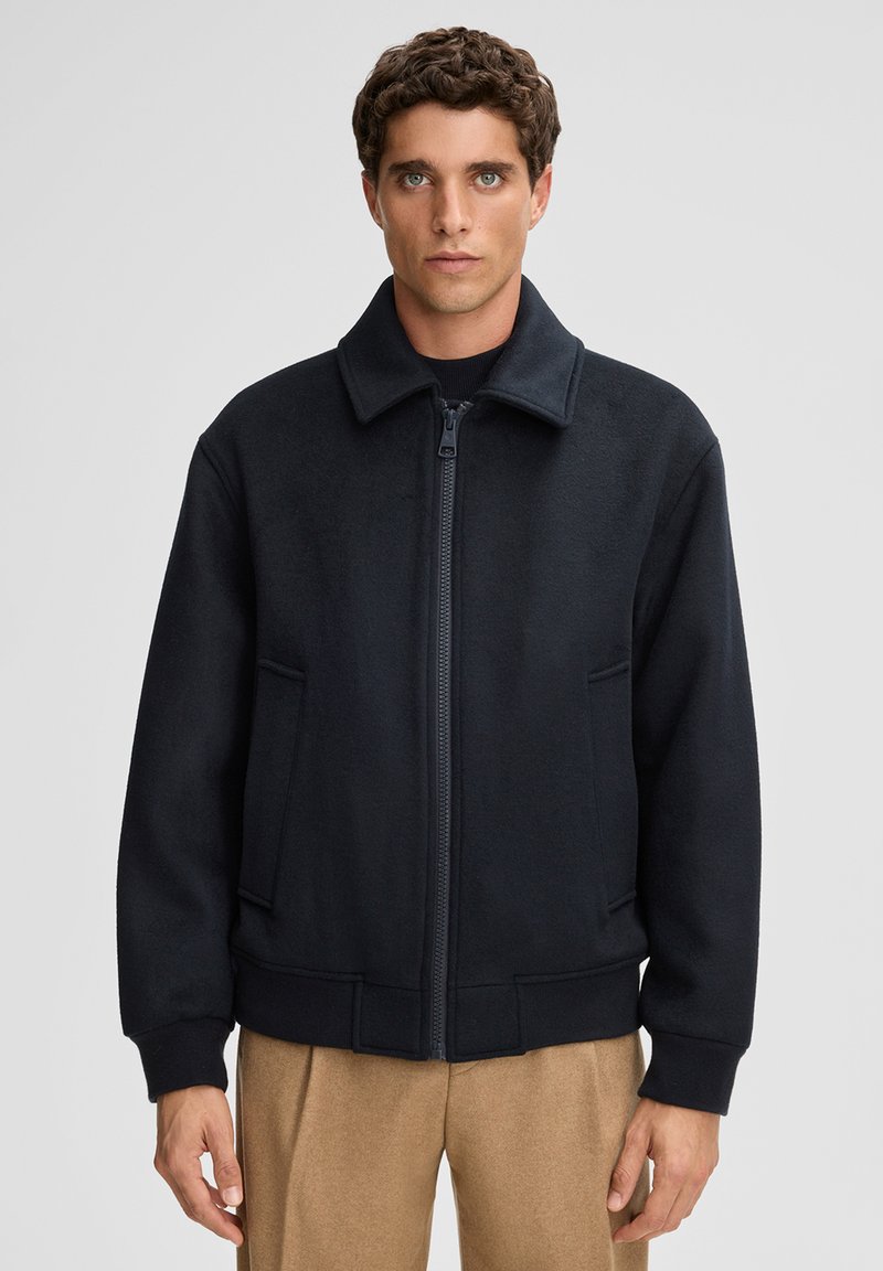 Black wool-blend jacket with a zip front, large collar, and side pockets. Features a relaxed fit and ribbed cuffs for texture.