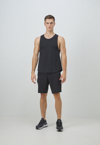Svart atletisk linne och shorts, tillverkade av lättviktsmaterial. Linnet är ärmlöst med en rundad fåll, kombinerat med svarta sneakers.