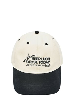 Casquette de baseball avec une calotte blanche et une visière noire, avec texte brodé noir "KEEP LUCK CLOSE TODAY AND TRUST THE PROCESS EST.1991."