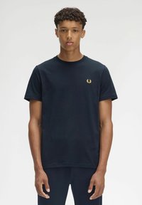 Camiseta de algodón azul marino con cuello redondo, mangas cortas y un pequeño logo de laurel dorado en el lado izquierdo del pecho. Textura suave y ajuste clásico.