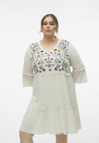 Vestido color crema con bordados florales en el canesú, escote en forma de V y mangas acampanadas. Presenta una falda de capas con acentos con volantes.