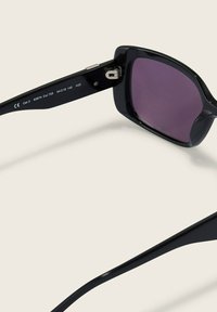 Schwarze Sonnenbrille mit rechteckigem Rahmen und dunkelvioletten Linsen. Verfügt über ein Scharnierdesign und gravierte Details an den Bügeln.