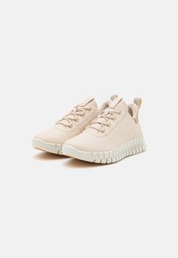 Scarpe da ginnastica beige chiaro con una tomaia sintetica liscia, linguetta testurizzata e suola bianca flessibile con un design ondulato.