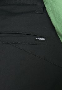 Pantalons noirs featuring a small Volcom logo tag, avec une texture lisse et des détails de couture subtils près de la poche.