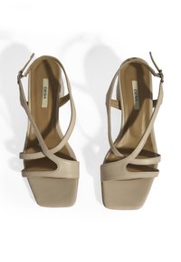 Beige sandaalhakken met brede banden, vierkante neuzen en een enkelgesp. Glad lederen textuur met minimale details.