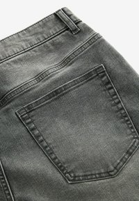 Jeans de mezclilla gris con un bolsillo trasero con un contorno cosido, textura claramente visible y sutiles variaciones en el color.