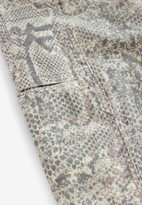 Grå og beige slangemønsterstof med en tekstureret overflade, der har en foldet fald og synlige syninger.