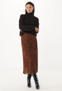 Suéter de cuello alto tejido en marrón oscuro combinado con una falda midi de estampado de leopardo naranja. Botines negros de tobillo completan el conjunto.