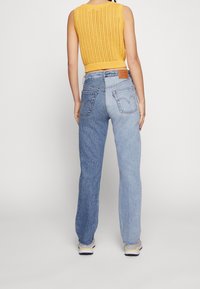 Slitna blå denimjeans med en tvåtondesign; ljusare tvätt till vänster, mörkare till höger. Har en lapptäck på baksidan och fem fickor.