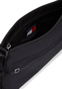 Μαύρη τσάντα από νάιλον με φερμουάρ, με λεία υφή, διακριτικό σχέδιο και εσωτερική ετικέτα με έμβλημα σε κόκκινο, λευκό και μπλε χρώμα.