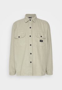Lekko zielona koszula sztruksowa z długimi rękawami, dwoma kieszeniami na piersi, zapięciem na guziki i małą metką na lewej kieszeni.