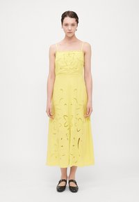 Vestido amarillo con tirantes de espagueti ajustables, con cortes florales y una silueta fluida. Combinado con unas planas negras con tachuelas.