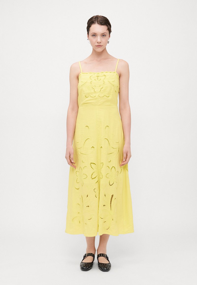 Vestido amarillo con tirantes de espagueti ajustables, con cortes florales y una silueta fluida. Combinado con unas planas negras con tachuelas.
