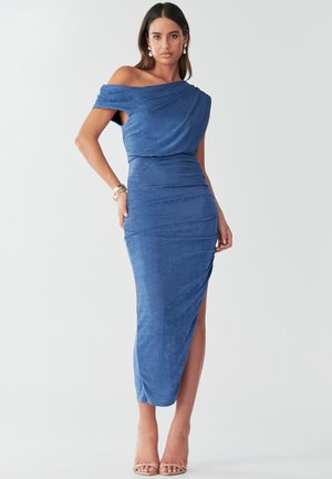 Modra obleka z odkrito rameni, z drapirano ovratnico, prilegajočim dizajnom in stransko razpiko. Mehka tkanina z diskretno teksturo. Oblečena z bež petami.