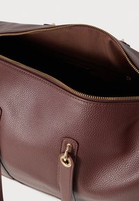 Hnedá kožená kabelka s hrubou štruktúrou, vybavená zlatým zipsom, jemnou vnútornou podšívkou a dvojitými rukoväťami pre všestranné nosenie.