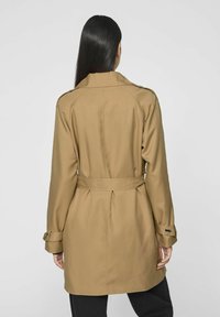 Beige trenchcoat med bälte i midjan, långa ärmar och axelremmar. Slät textur med rak passform och inga synliga mönster.