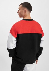 Fargeblokkert sweatshirt med røde, svarte og hvite paneler; laget av myk stoff med rund hals og ribbestrikkede mansjetter.