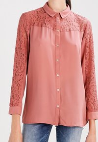 Růžová blůza s krajkovými rukávy a zapínáním na knoflíky. Obsahuje límec, dlouhé rukávy a hladkou texturu.