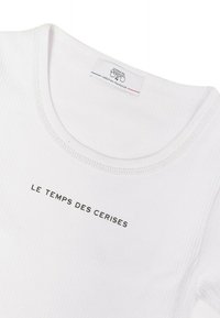 T-shirt en coton blanc à côtes avec un col rond et des manches courtes, présentant le texte "LE TEMPS DES CERISES" en noir sur le devant.