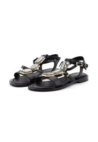 Sandali in pelle nera con suola piatta, molteplici cinturini e dettagli decorativi a strisce dorate e bianche sulla parte superiore.
