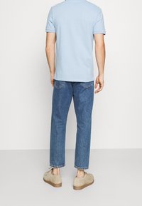 Polo shirt in cotone azzurro chiaro, vestibilità rilassata, maniche corte. Abbinato a jeans in denim blu scuro, leggermente affusolati, orlo sfilacciato, calzature beige.