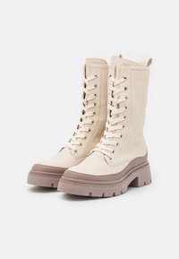 Bottes en cuir crème montantes avec une semelle épaisse taupe, bout arrondi et fermeture à lacets à l'avant, dotée d'œillets en métal et d'un col rembourré.