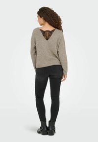 Grijze trui met een V-hals en kantdetails op de rug, gecombineerd met zwarte skinny jeans en zwarte enkellaarsjes. Geweven breimateriaal.
