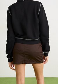 Černý zkrácený sweatshirt s šedými prošívacími detaily. V kombinaci s hnědou mini sukní. Materiál vypadá měkký s běžným střihem.