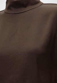 Gros plan d’un tissu lisse brun foncé avec un col montant, probablement une partie d’un vêtement ou d’un pull.