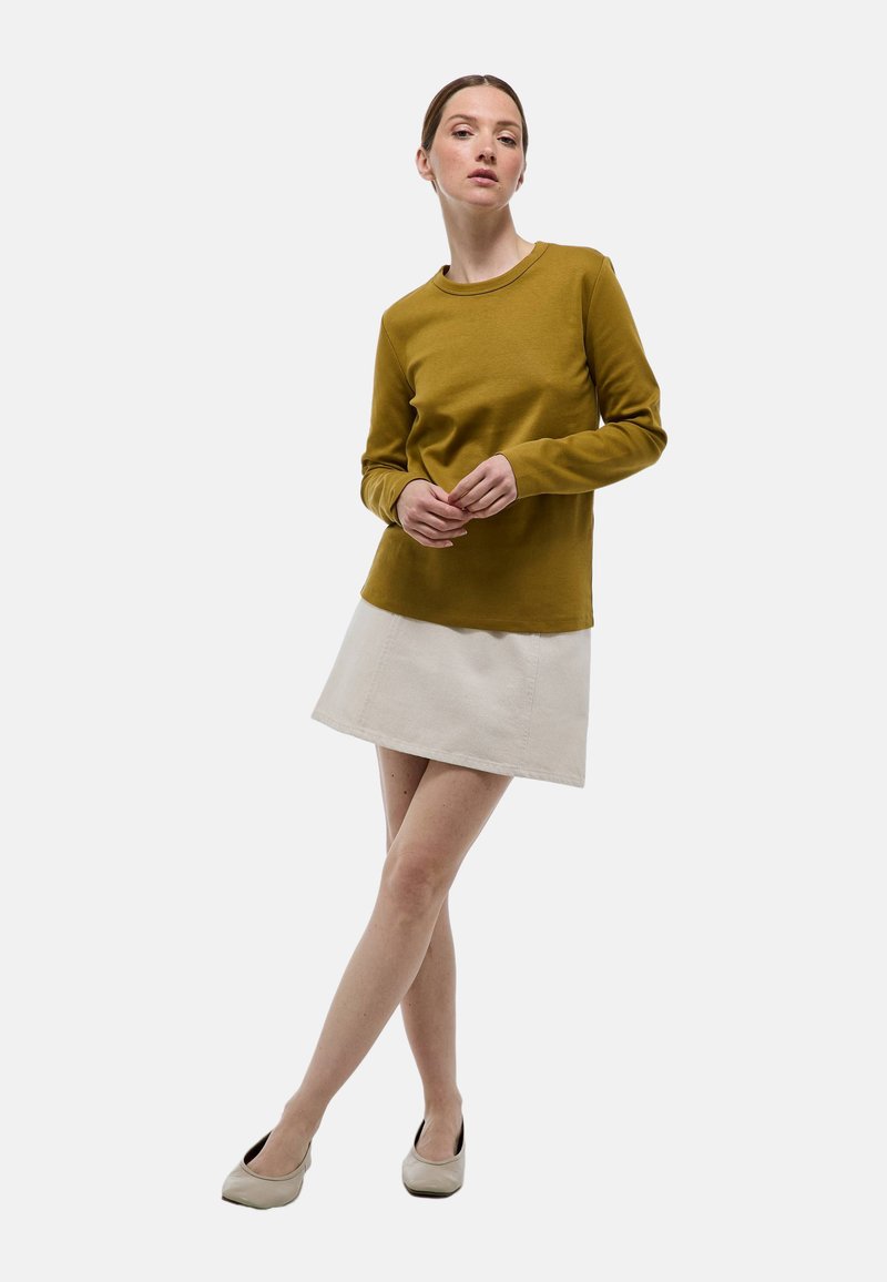 Chemise à manches longues moutarde assortie à une mini-jupe beige clair. Les textures douces et le design simple soulignent un look décontracté.