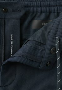 Tissu texturé bleu marine foncé avec bouton, fermeture éclair et détails de cordon noir et blanc sur vêtement de sport.