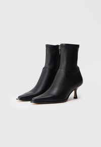 Botas de cuero negras hasta el tobillo con puntera afilada, cierre con cremallera y tacón delgado. Textura suave sin patrones ni acentos visibles.