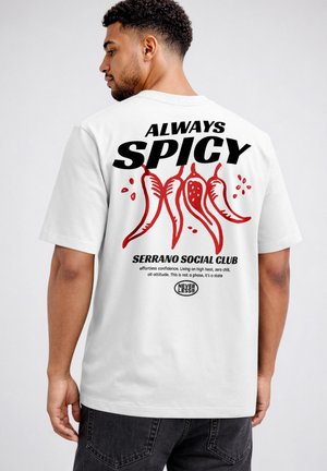 Man wearing a white T-shirt with red chili peppers and the text "Always Spicy Serrano Social Club" on the back.