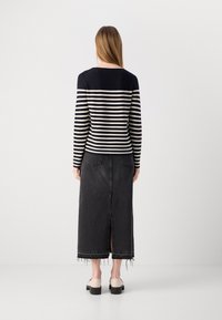 Csíkos kötött pulóver tengerészkék és krém színben, párosítva egy hosszú fekete farmer szoknyával, középső hasítékkal és rojtolt szegéllyel.