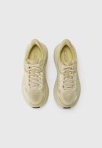 Zapatillas deportivas beige con parte superior de malla, punta redonda y cordones planos. Presentan un ligero acolchado y acentos de suela de goma negra.