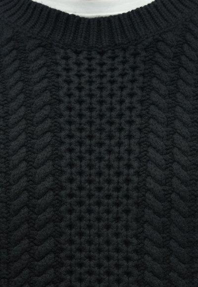 Κοντινή λήψη μαύρου πλεκτού πουλόβερ με σχέδια ζικ-ζακ και υφασμένα μοτίβα, και ριμπ λαιμόκοψη.