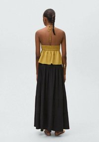 Haut halter smocké jaune moutarde associé à une longue jupe noire à volants. Texture lisse, dos ouvert et liens de cou ajustables.
