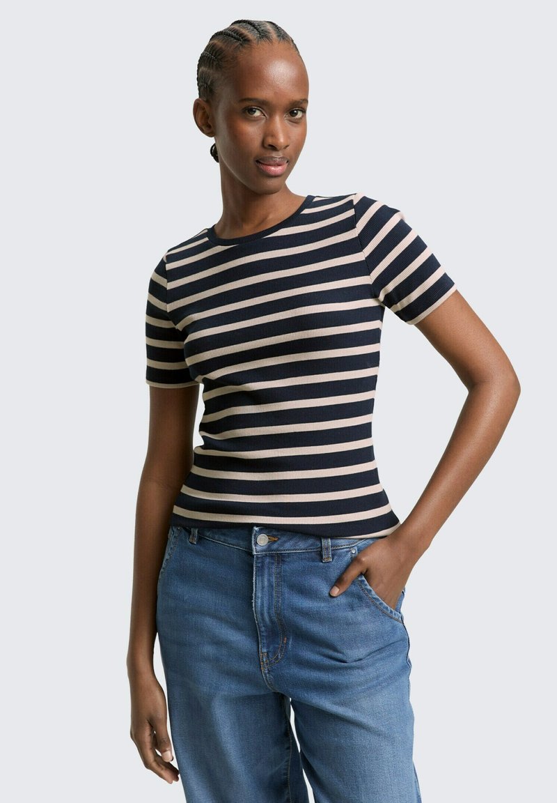 Krótki rękaw, dopasowana koszulka z poziomymi paskami w kolorze granatowym i beżowym, o prążkowanej fakturze i okrągłym dekolcie. Połączona z luźnymi niebieskimi dżinsami.