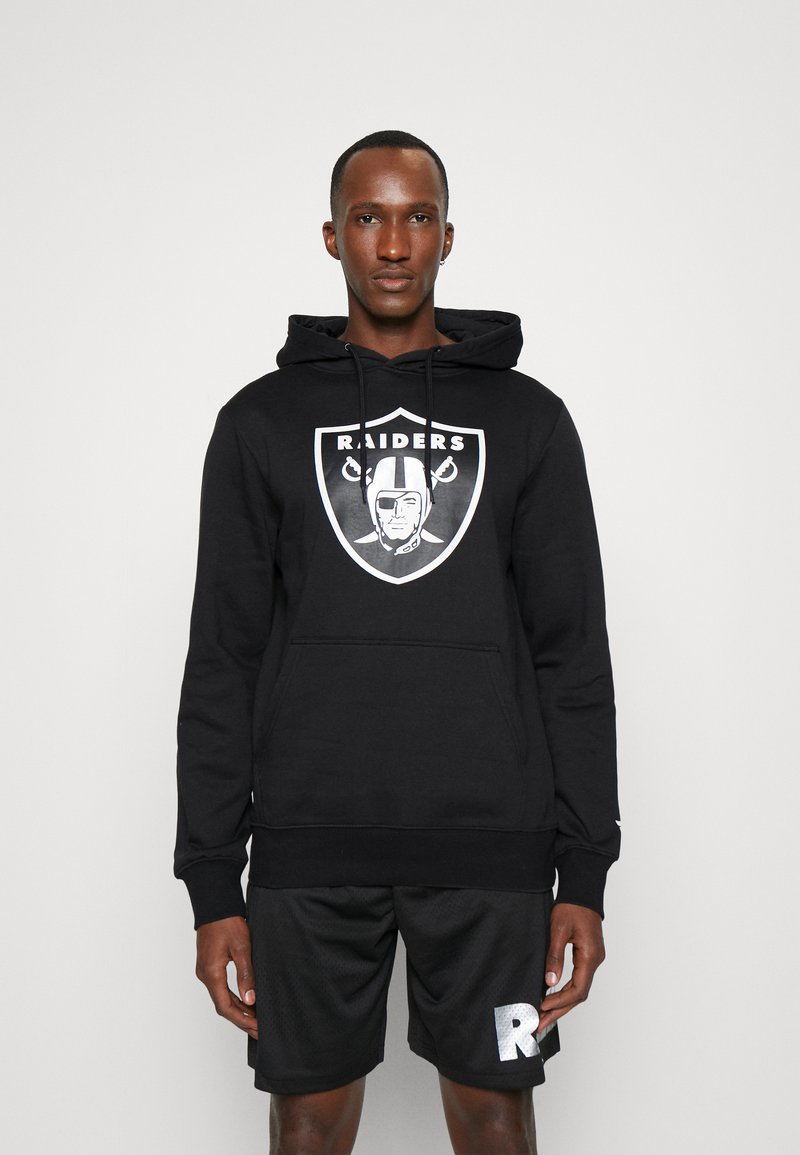 Sudadera negra con el logo de los Raiders, con un bolsillo canguro, capucha con cordón y puños acanalados. Llevada con pantalones cortos negros que presentan un logo blanco.