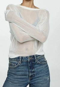 Maglione bianco in rete con vestibilità ampia e scollatura larga, abbinato a jeans in denim blu a vita alta con un finish scolorito.