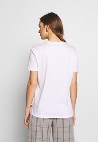 Weißes Baumwoll-T-Shirt mit kurzen Ärmeln, Rundhalsausschnitt und seitlichem Schlitz, kombiniert mit hellen Karohosen.