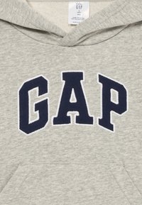 Felpa grigia in misto cotone con il logo "GAP" in blu navy ricamato in rilievo. Presenta una tasca a marsupio e un cappuccio regolabile con cordino.