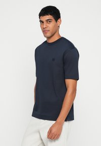 Granatowy t-shirt z krótkim rękawem wykonany z miękkiego materiału, z okrągłym dekoltem i małym logo na lewej piersi.