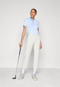 Strój golfowy składający się z jasnoniebieskiej koszulki polo z kołnierzykiem i drobnym wzorem, beżowych spodni oraz jasnoszarych butów golfowych z zielonymi akcentami.