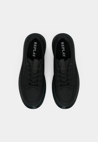 Baskets noires avec une texture lisse, une forme arrondie, un bout perforé et des lacets plats. Elles présentent un logo sur la languette et une semelle rembourrée.