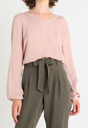 Langærmet bluse i blush pink med v-hals og tekstureret stof, parret med højtaljede grønne bukser med bindebånd.