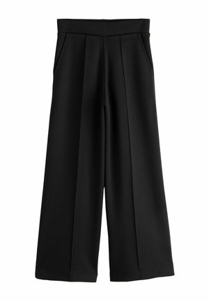 Hand resting inside the pocket of black pants, showing part of the waist and hip area with a white shirt hem visible.