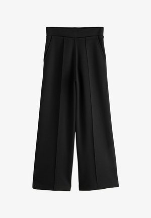 Hand resting inside the pocket of black pants, showing part of the waist and hip area with a white shirt hem visible.